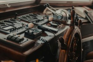 Vintage boat control panel with various gadgets and a wooden steering wheel.